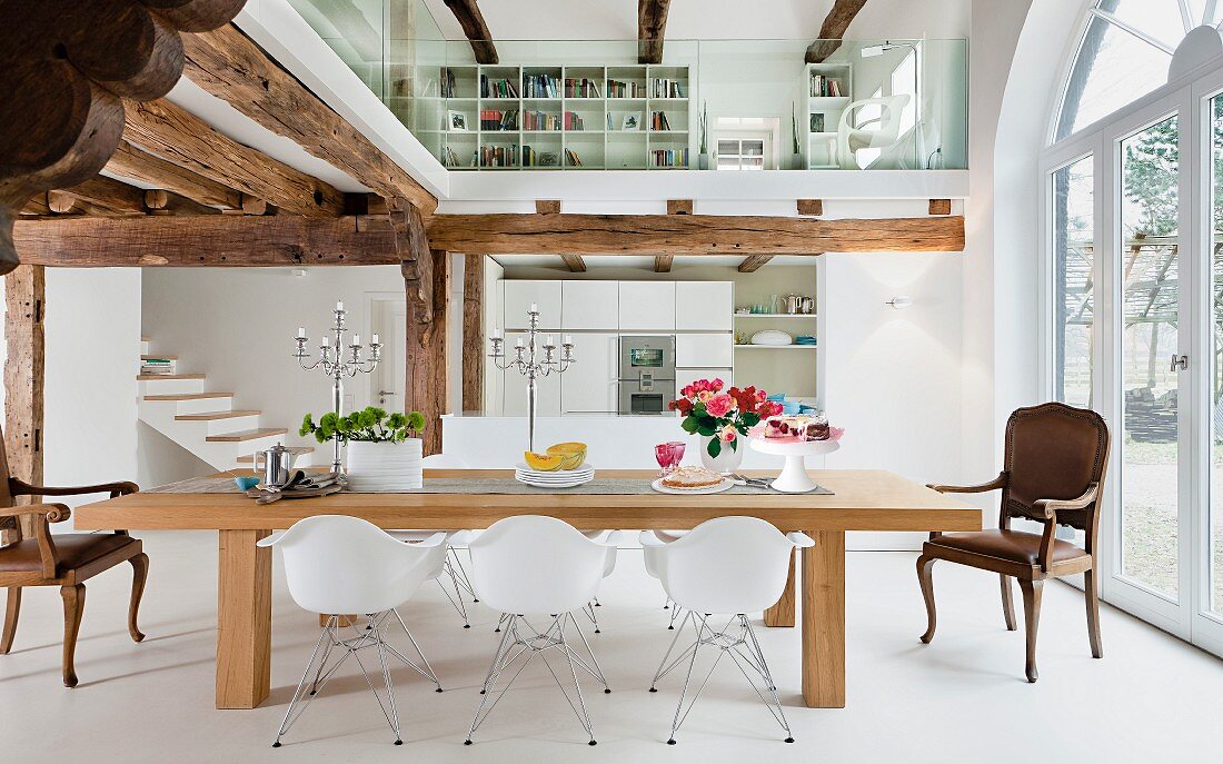 An open-plan dining room in white with a wooden beam ceiling and a glazed gallery