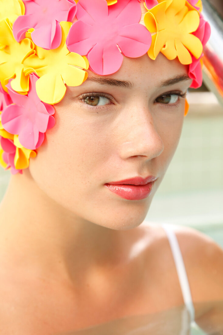 A woman wearing makeup with a colorful bathing cap looking into the camera