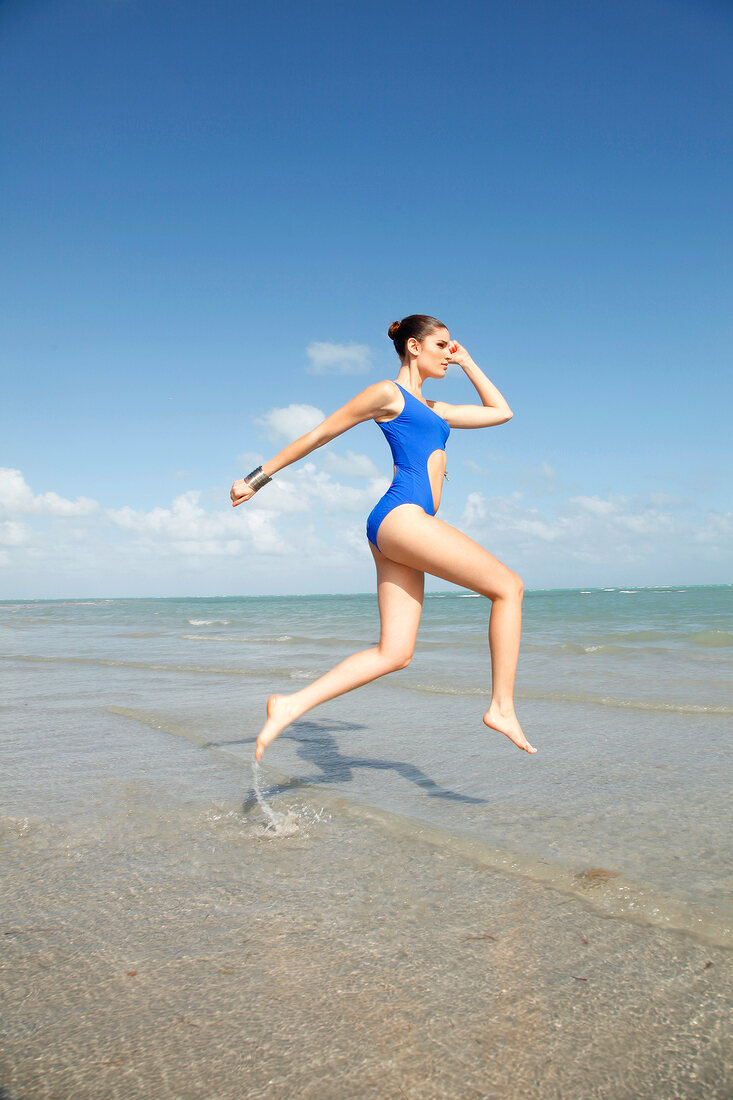 Frau im blauen Badeanzug macht einen Sprung am Strand