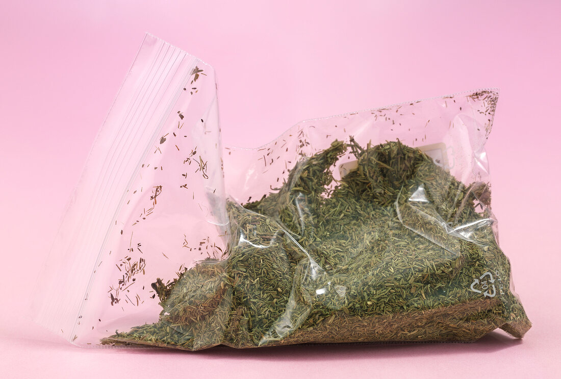 Dried herbs in bag on pink background