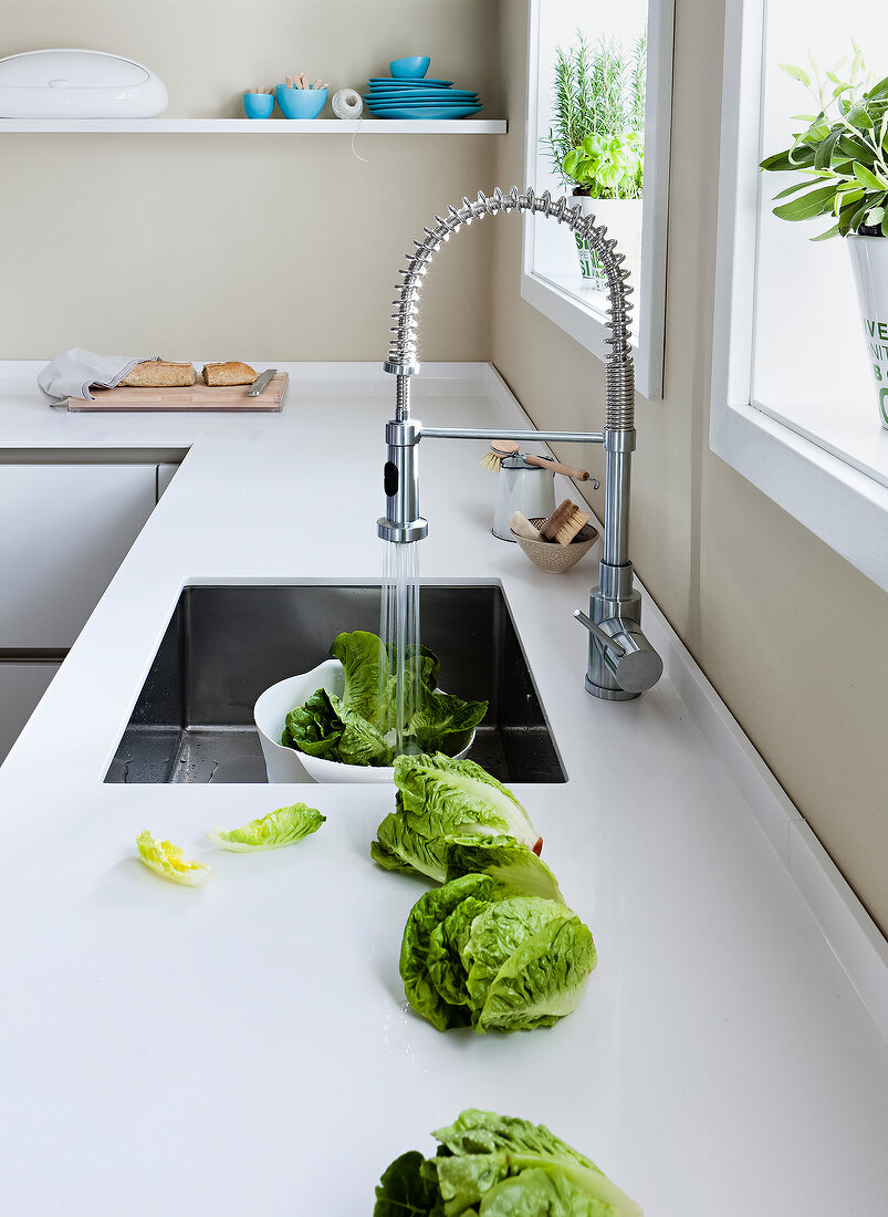 Lettuce leaves being washed under kitchen faucet at under mount sink