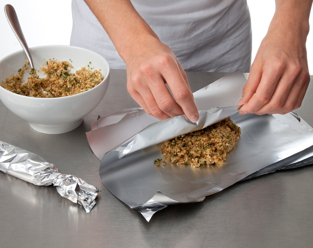 Close-up of hand wrapping sauteed bread crumbs and parmesan in aluminium foil, step 2