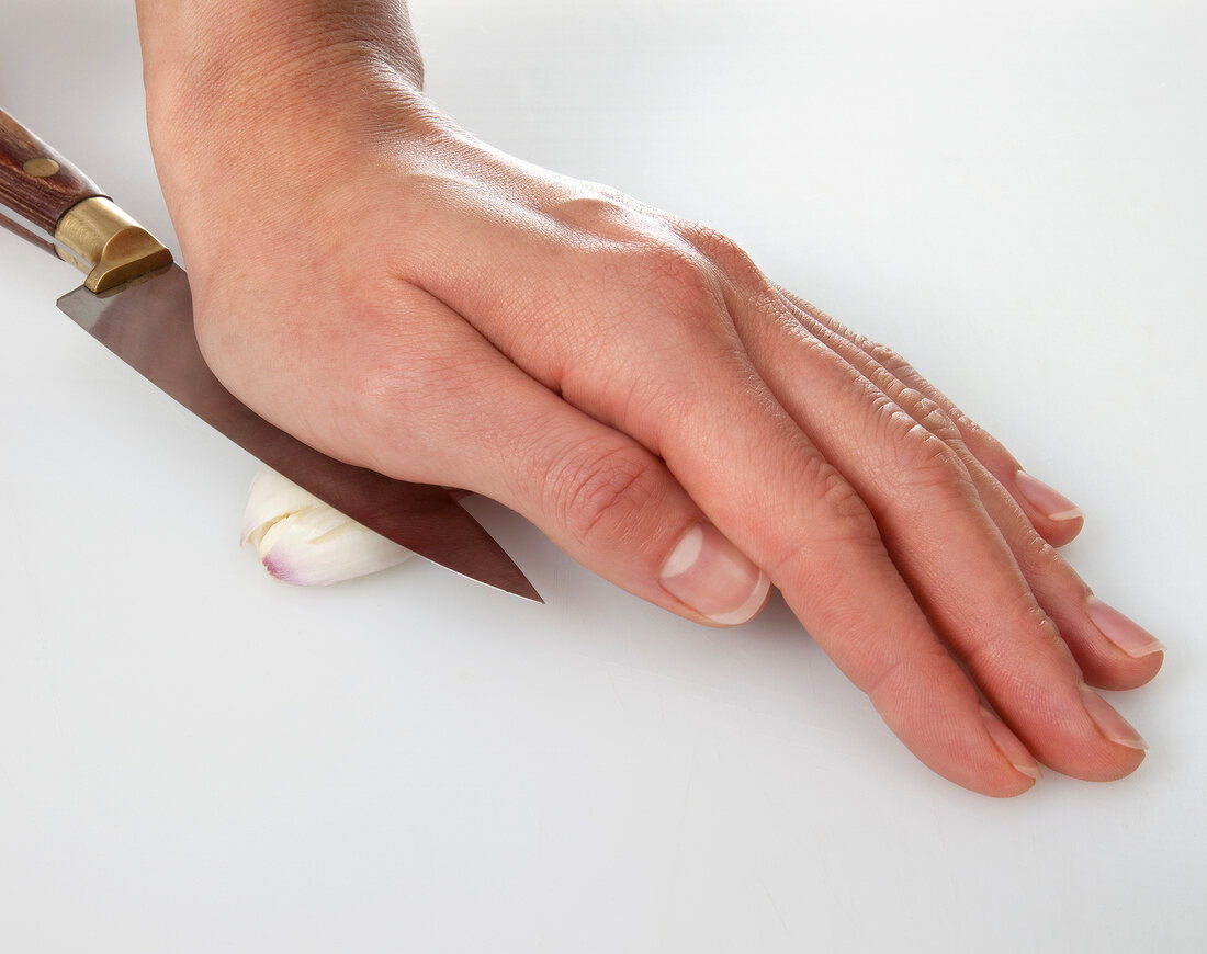 Garlic clove being crushed with knife on white background