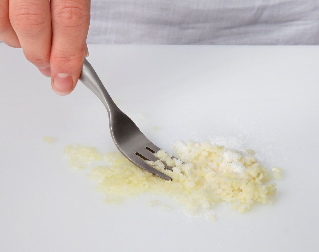Crushed garlic being loosened with fork on white background