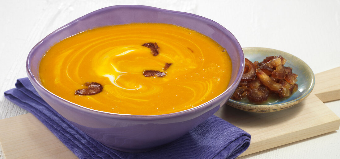 Pumpkin soup in bowl and dates on wooden serving board