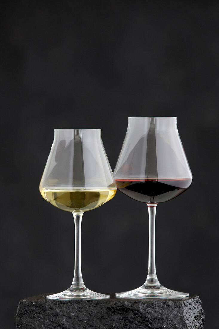 Two glasses with red and white wine against black background