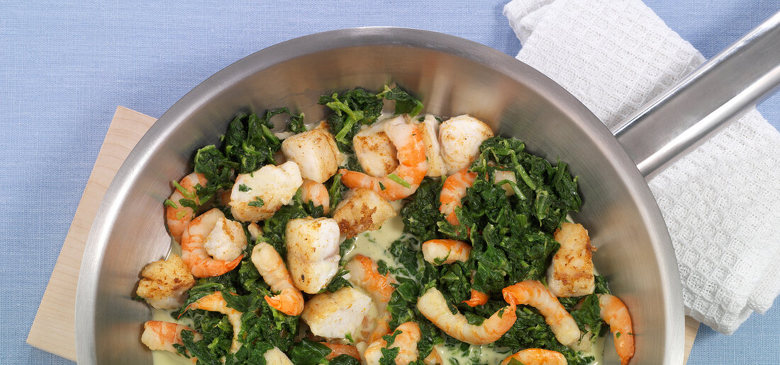 Close-up of fish and shrimp with spinach on pan