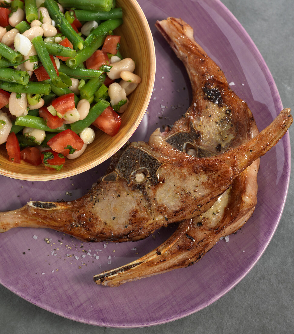 Lamb on plate with bean salad in bowl