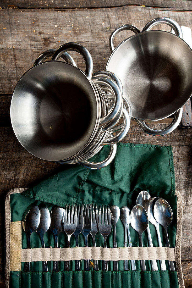 Stack of stainless steel bowls, pot and cutlery in pouch on table, elevated view