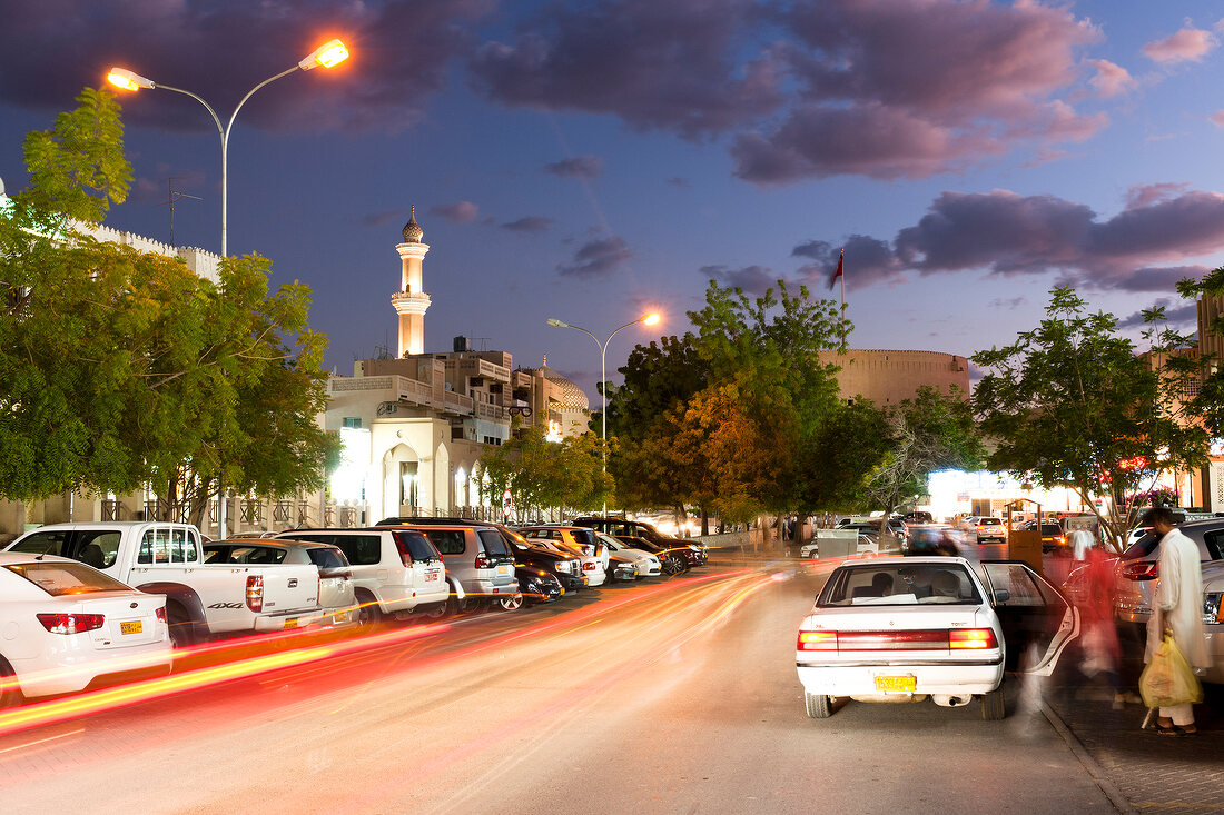 View of city street with cars and mosque in front at night in Nizwa, Oman