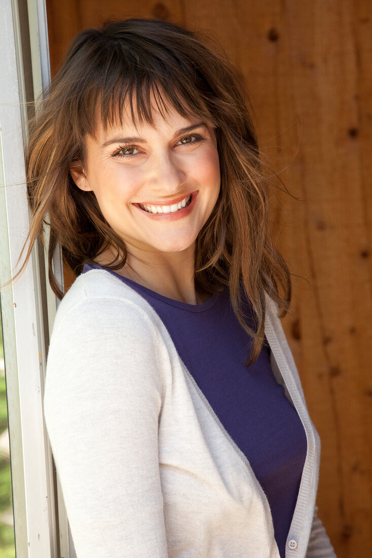 Portrait of pretty brown haired woman wearing purple top and white cardigan, smiling