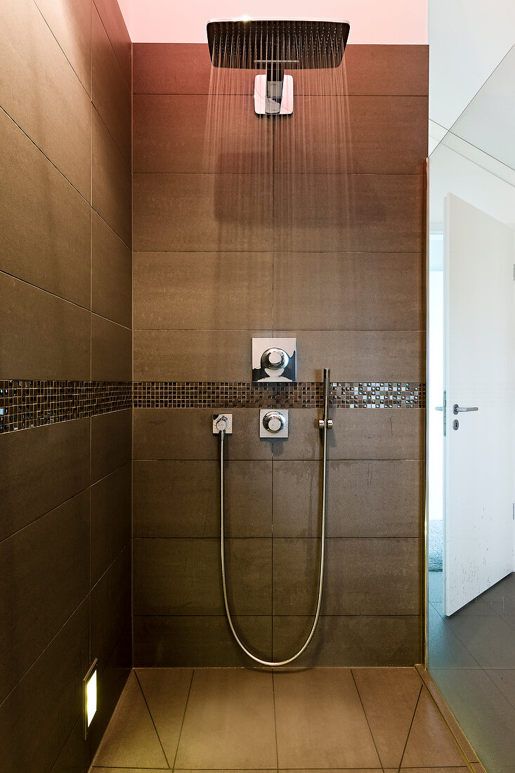 Head shower and water jet in brown tiled bathroom