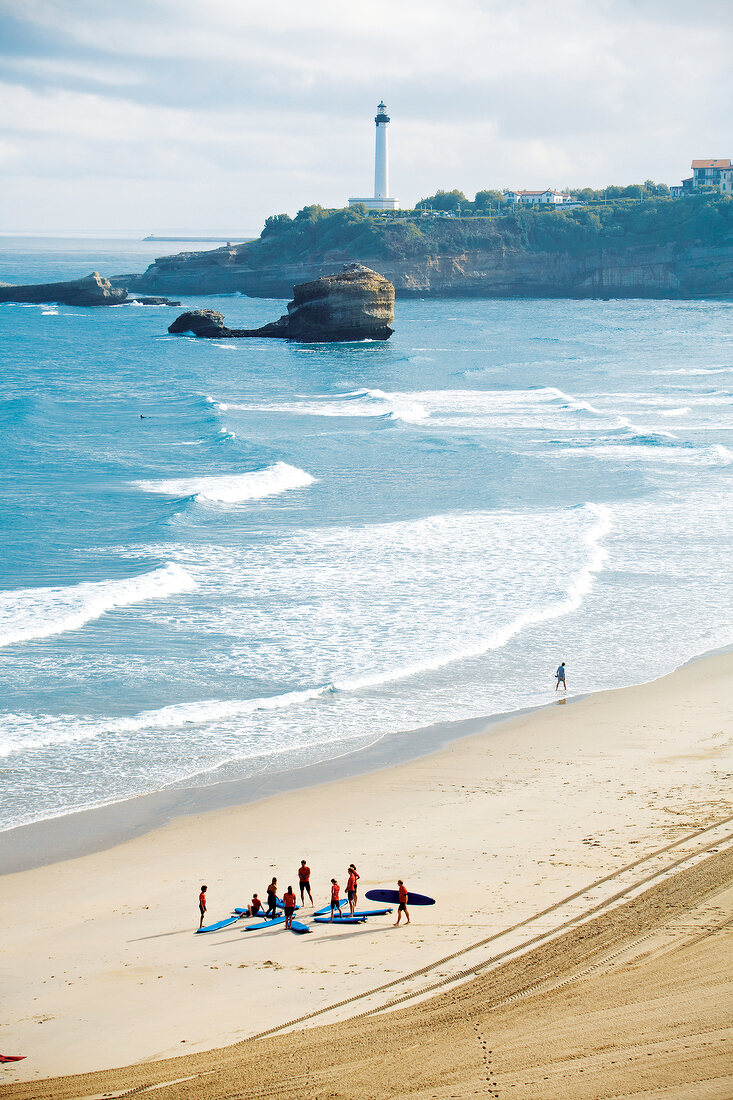 People with surf boards on beach in Biarritz, France