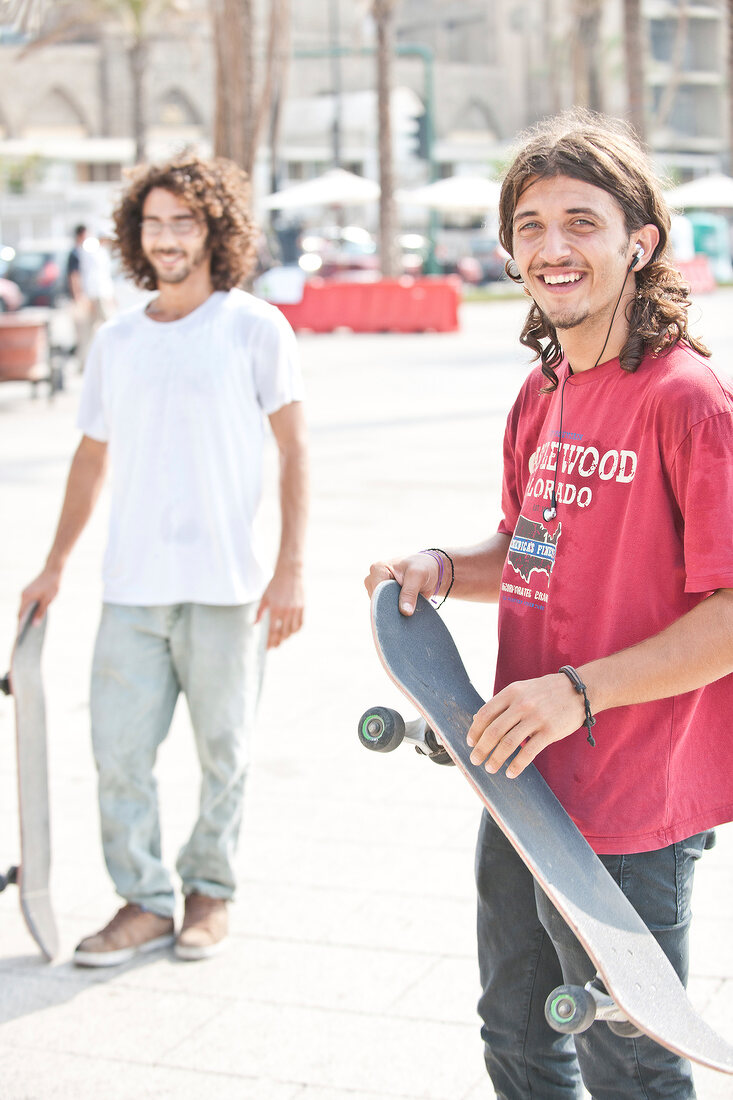 Two men in casuasl standing with skateboards on sidewalk, Beirut, Lebonan