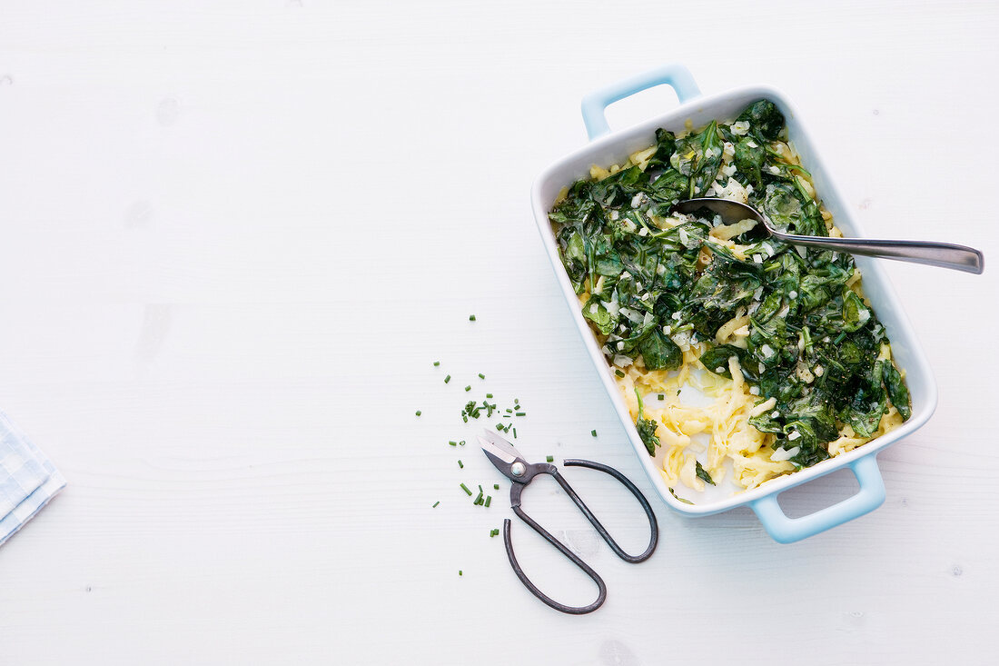 Cheese noodles with spinach in casserole on white background