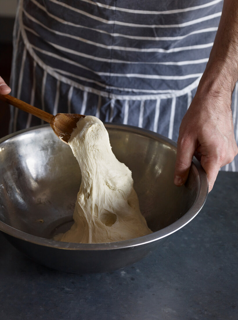 Baker using a wooden spoon to stir dough in mixing bowl stock