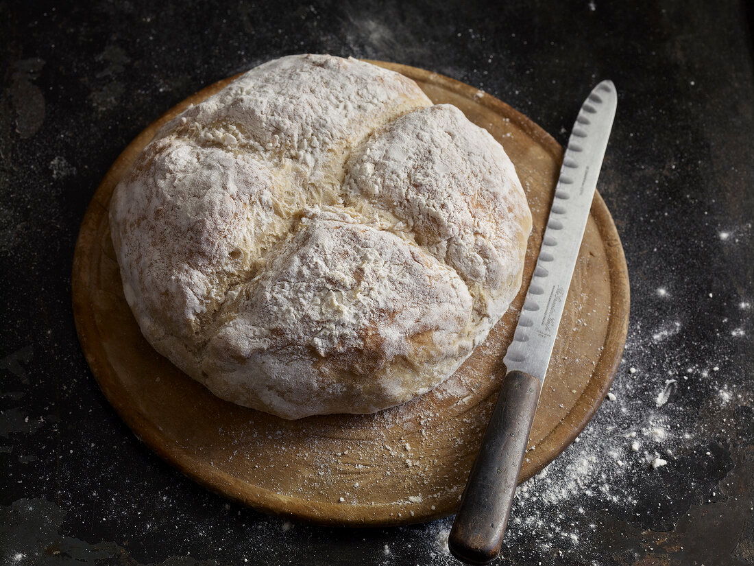 Loaf of beer bread on round wooden board with knife