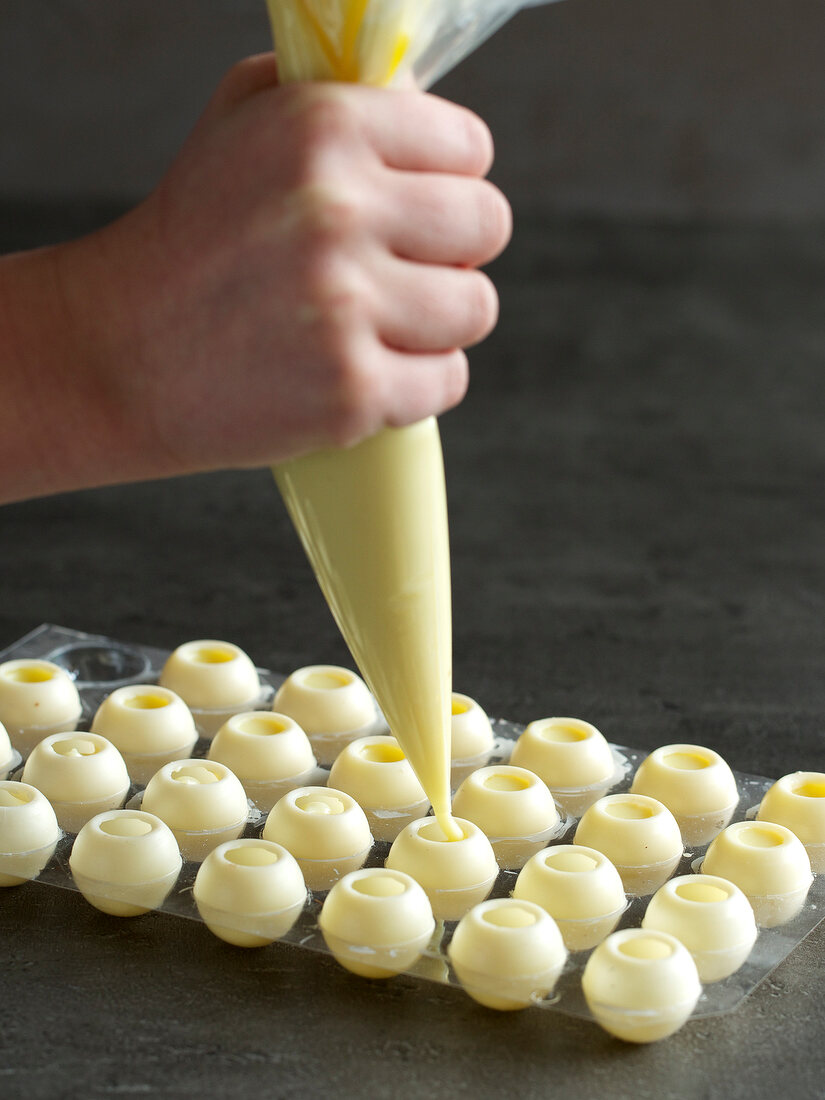 Close-up of hand filling cream with piping bag in absinthe balls, step 1