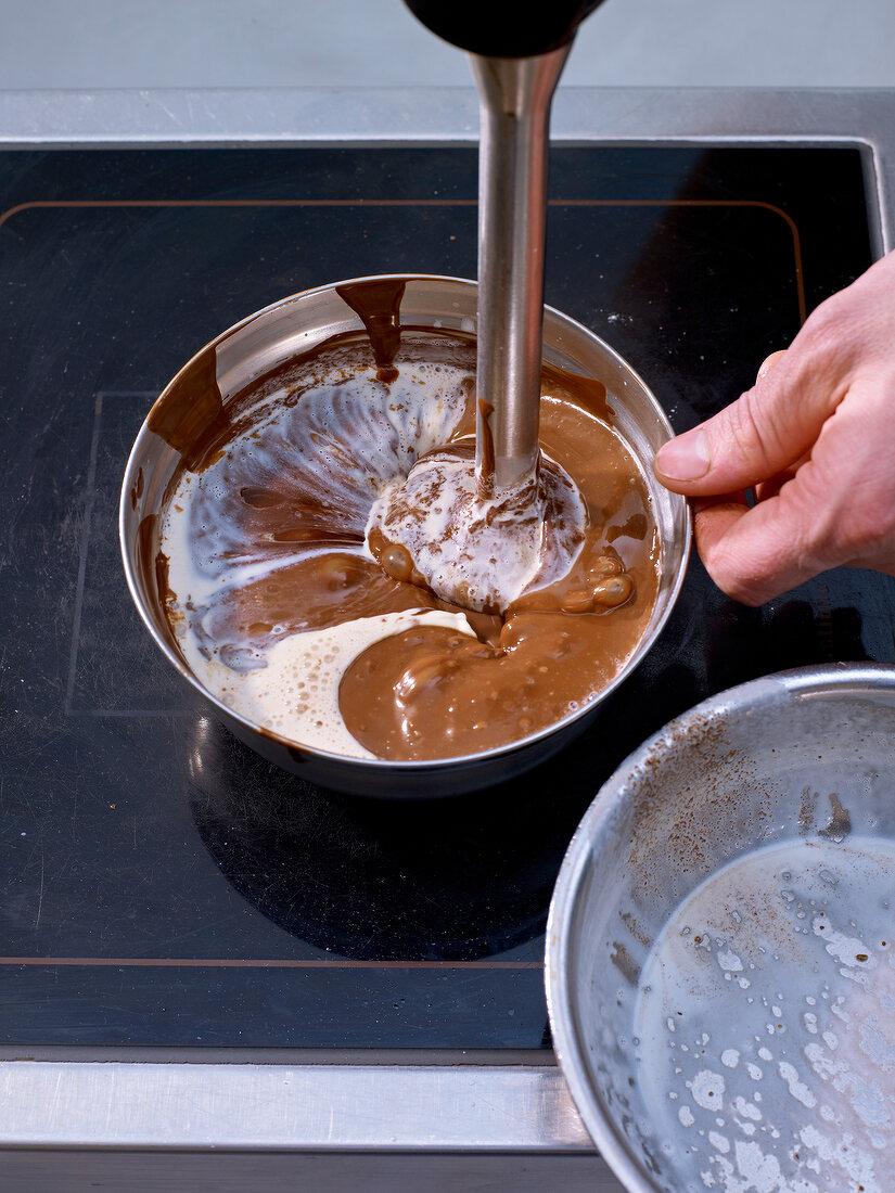 Mixing chocolate, nougat and cream with hand blender in bowl