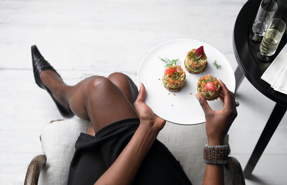 Dark-skinned woman holding plate of salmon tartare with avocado-taler, overhead view