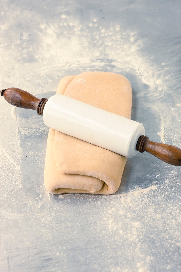 Rolling pin on folded dough with butter while preparing pastry, step 4