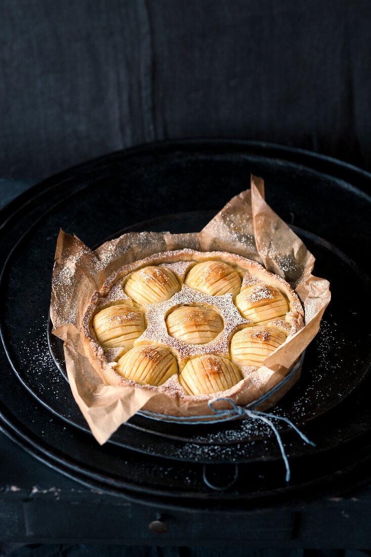 Apple pie with icing sugar in baking paper on black plate