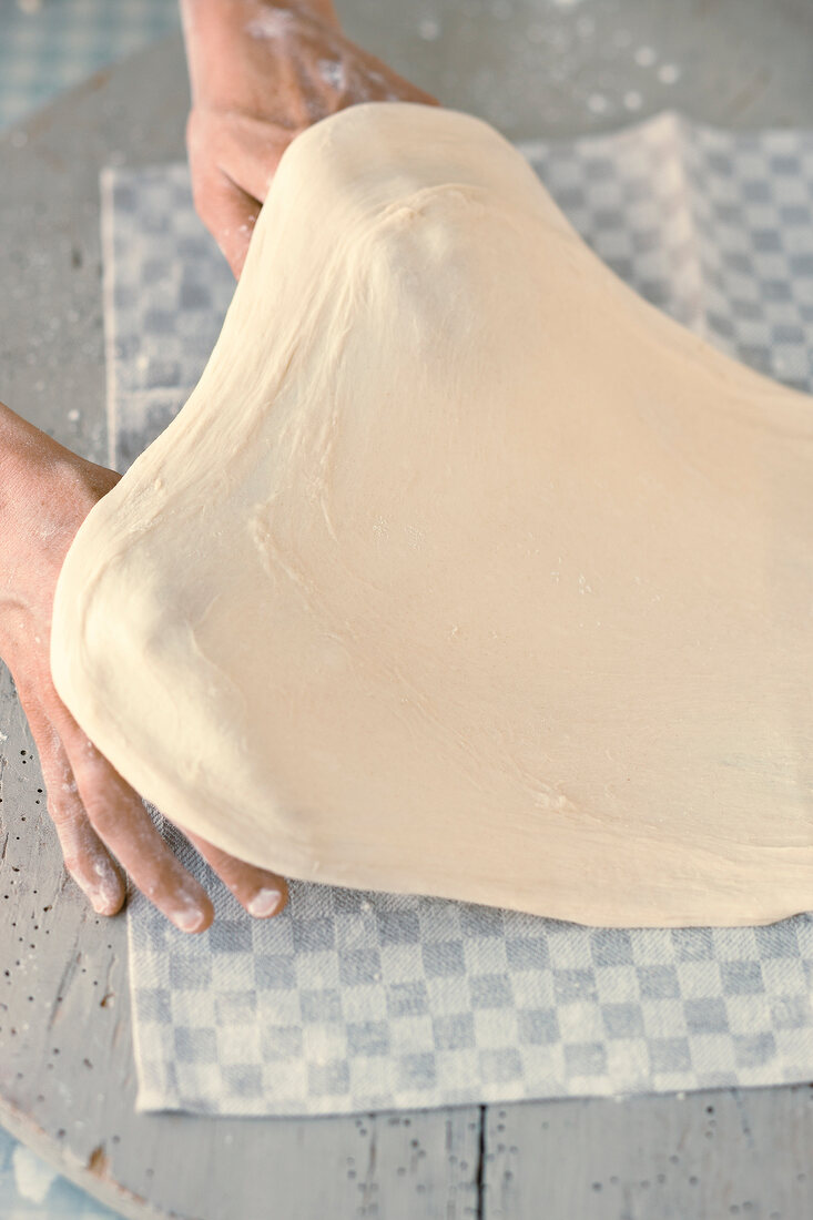 Close-up of hand stretching strudel dough to make it thin
