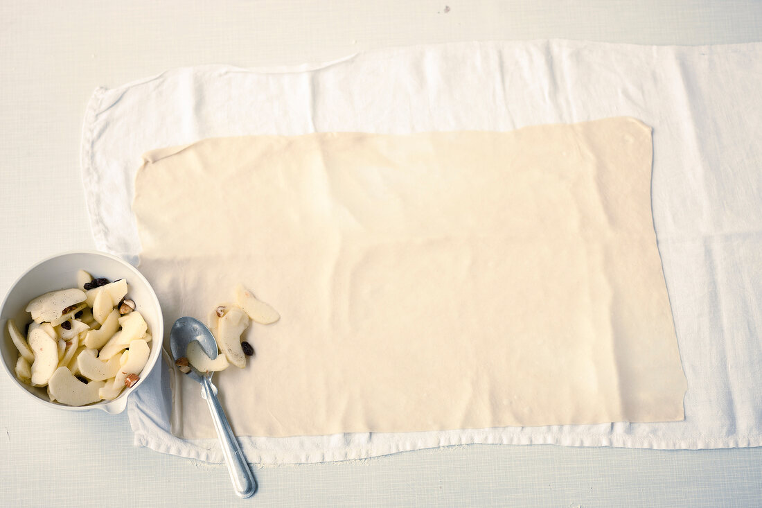 Ingredients being put on thin strudel dough for making apple strudel