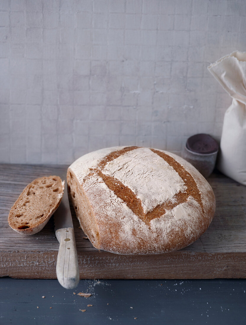 Loaf and slice of bread on wood board with knife