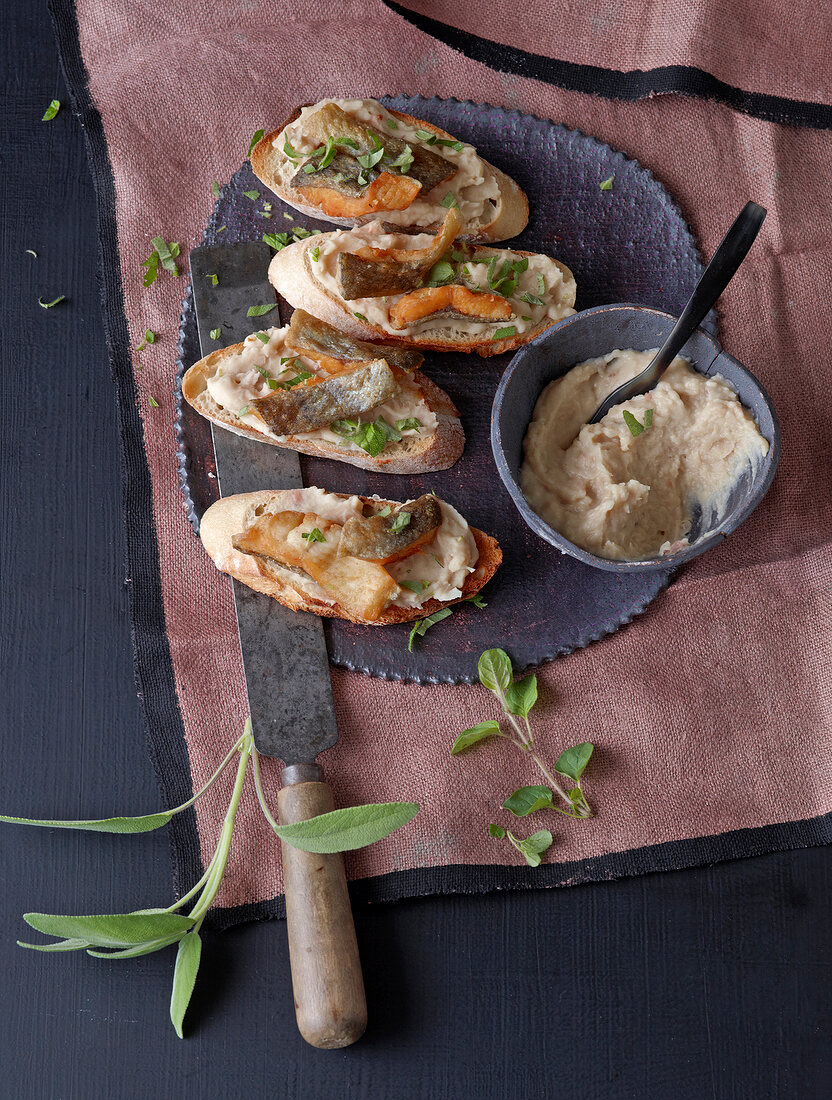 Four crostini with trout strips and bowl of bean cream on board