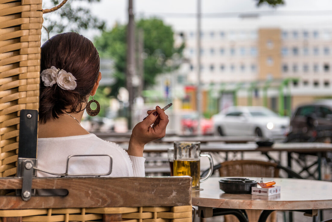 Rear view of woman holding cigarette and sitting on chair, Hannover, Germany