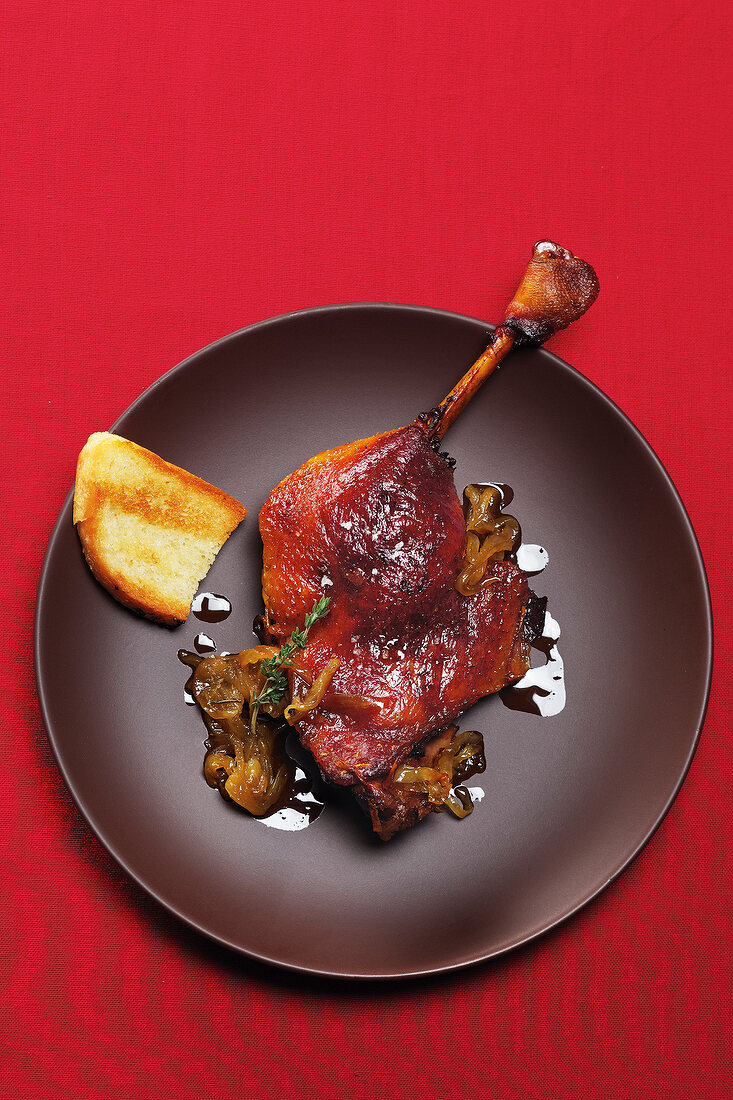 Goose leg confit with onion and garlic bread on plate, overhead view