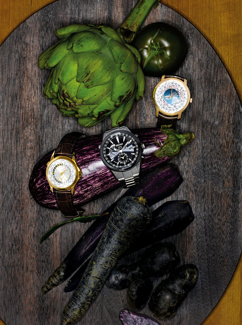 Watches, eggplant, artichoke roots and tomato on wooden surface