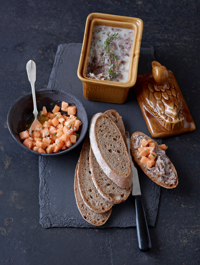 Bowl of duck rillettes and melon salad with bread on tray