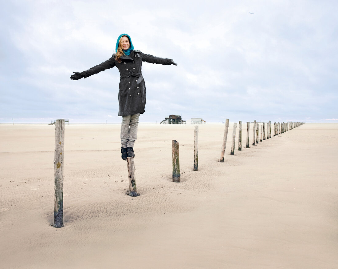 Woman wearing burberry coat balancing on stake at beach