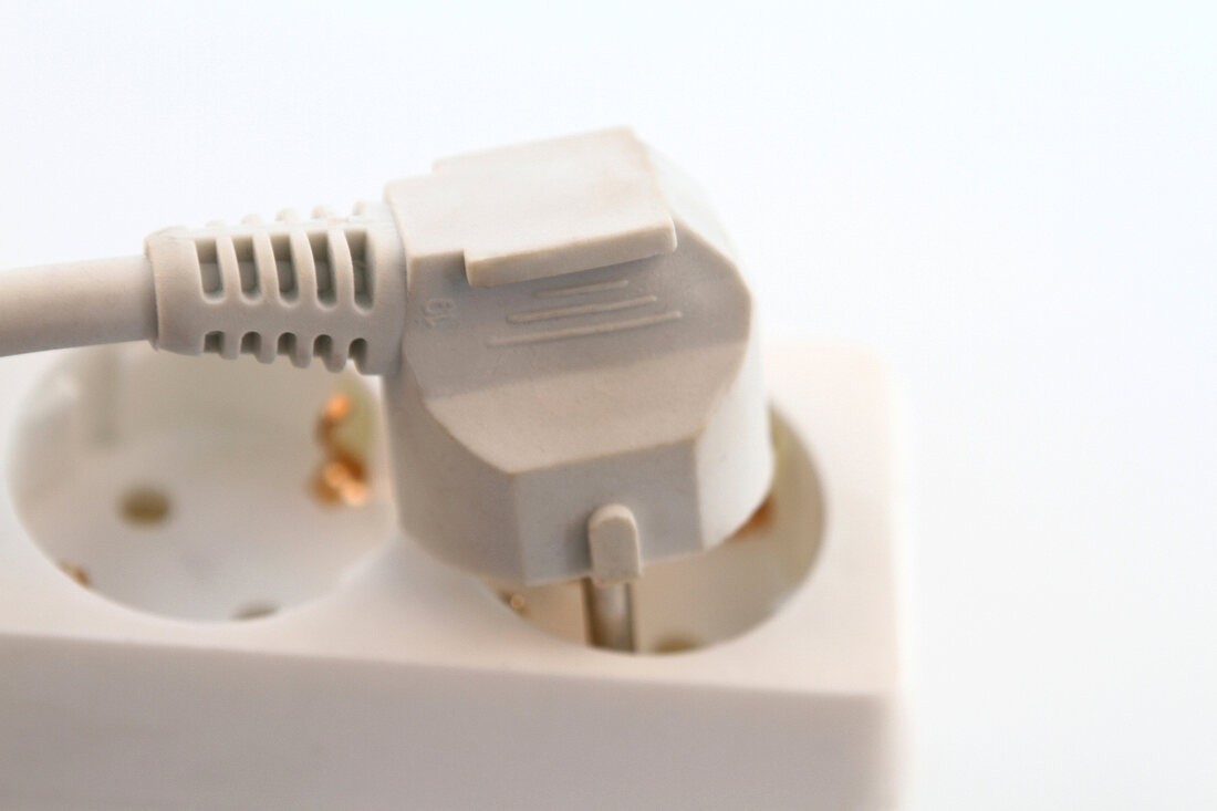 Close-up of plug on extension board against white background