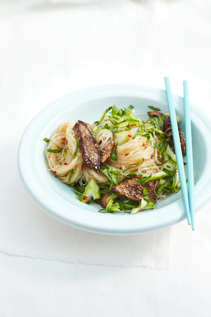 Noodle salad with sesame and beef on plate with chopsticks