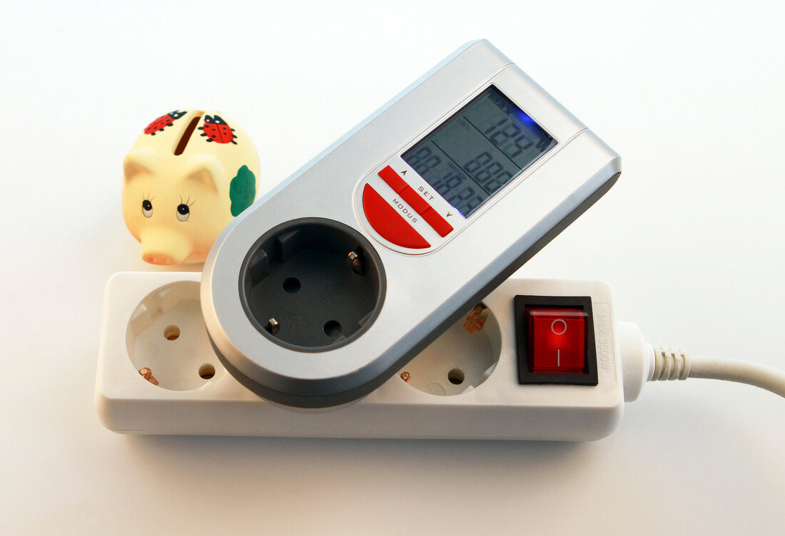 Close-up of triple plug extension with ammeter and piggy bank on white background