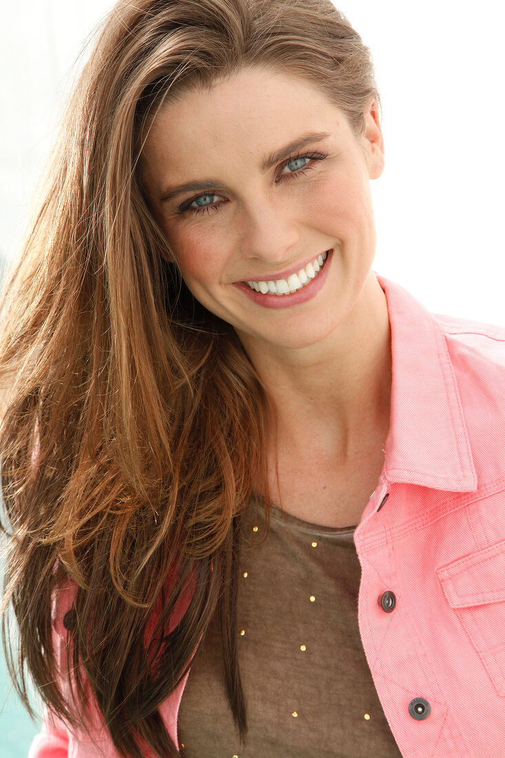 Portrait of pretty woman with dark hair wearing brown top and pink denim jacket, smiling