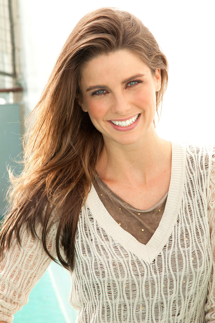 Portrait of pretty woman with dark long hair wearing brown top and sweater, smiling