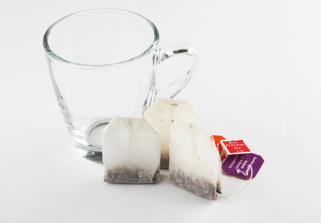 Glass tea cup with three tea bags on white background