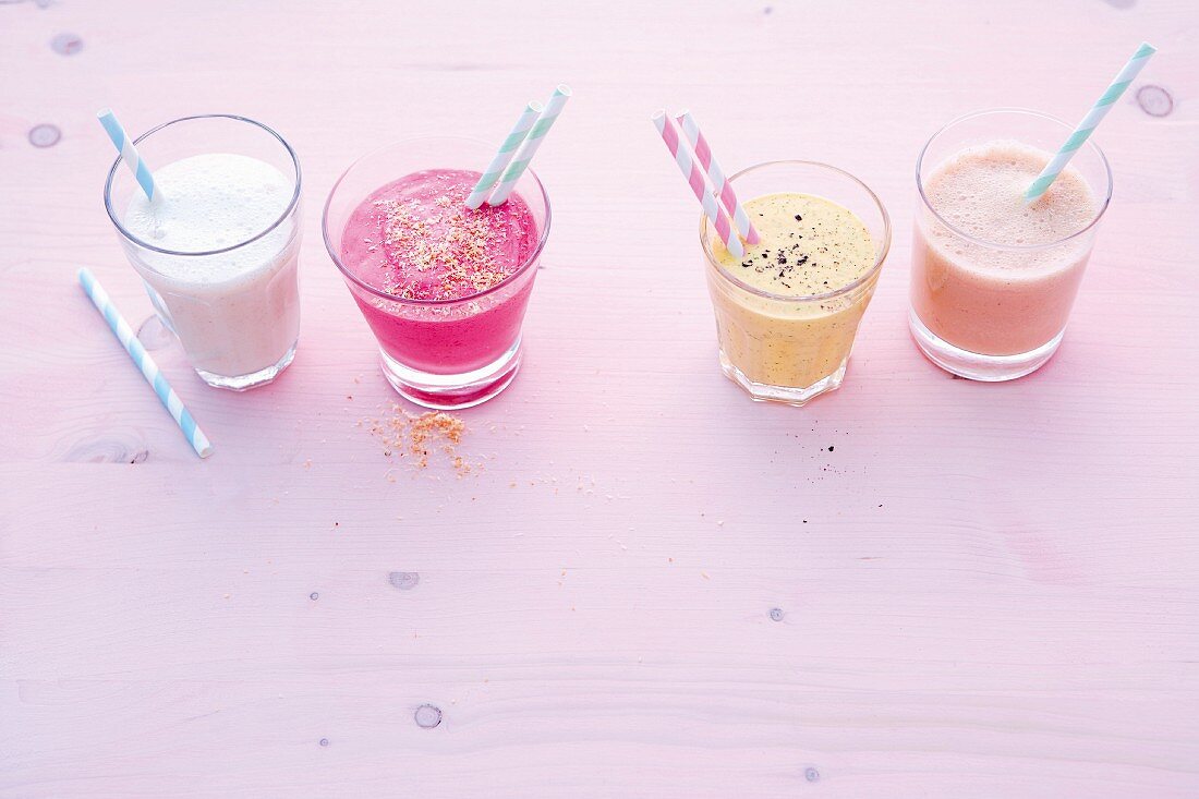 Four healthy smoothies in glasses with straws