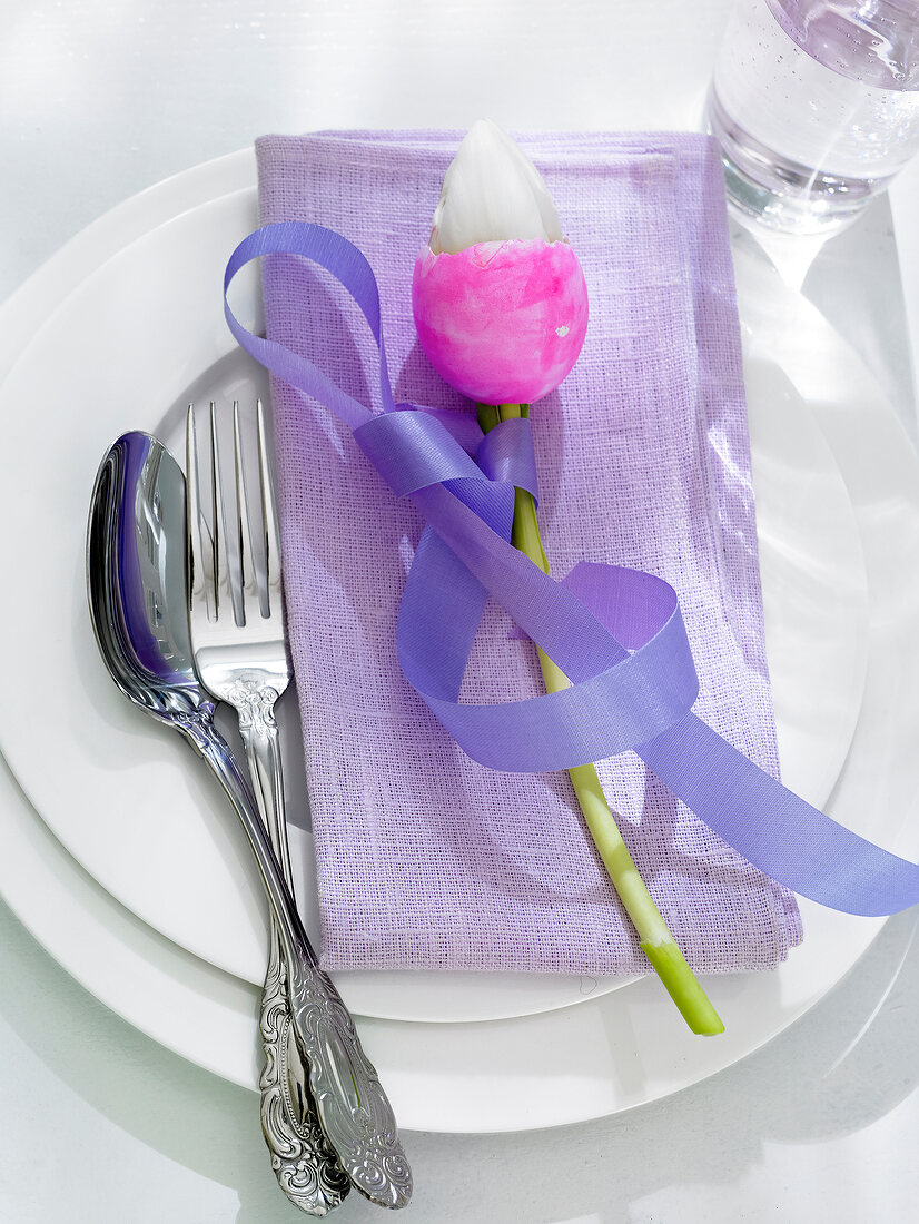 Easter egg enveloped in tulip and tied with purple ribbon on plate