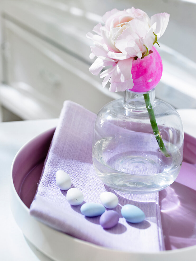 Mini Easter eggs in plate with flower in glass vase as Easter decoration