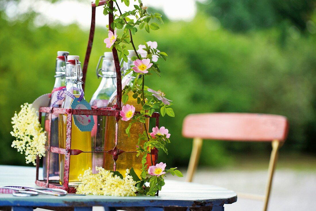 Sirupflaschen in Flaschenkorb aus Metall auf Gartentisch