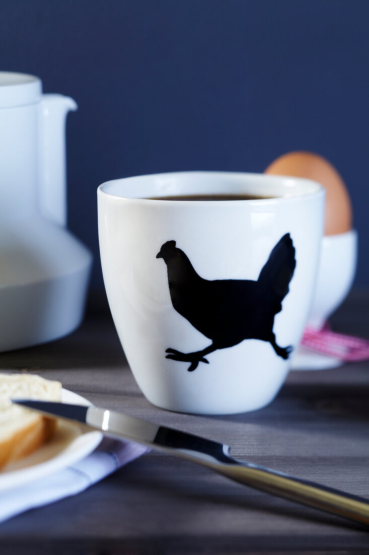 Kaffee im Becher mit Huhnmotiv und Frühstückstisch