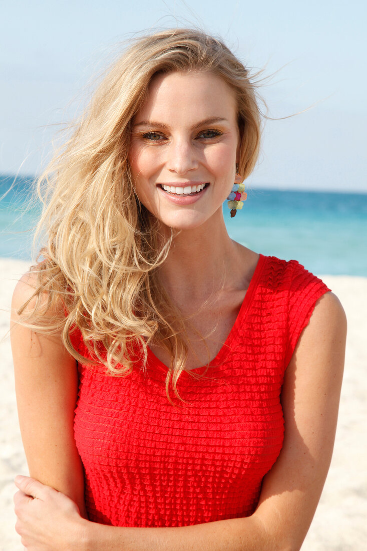 Blonde woman in a red dress on the beach, smiling and looking at camera