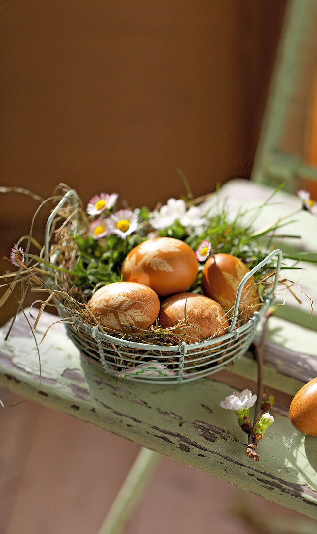 Close-up of metal basket with straw, daisies and eggs