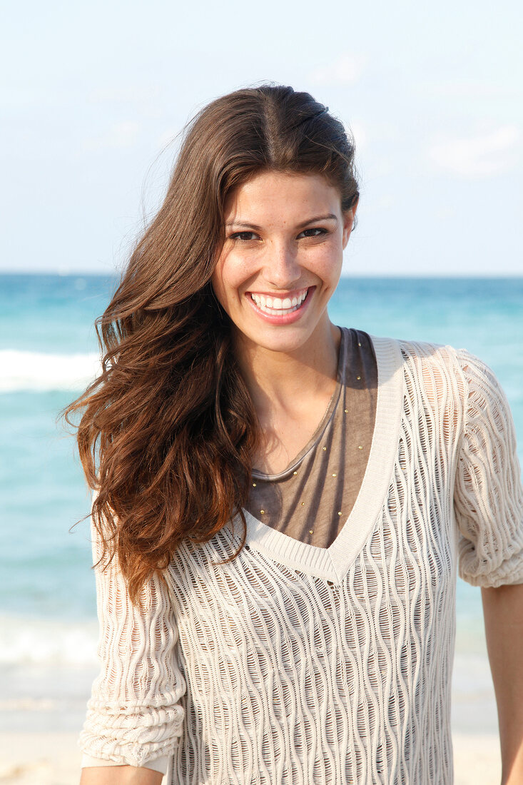 Dark-haired woman in a V-neck mesh sweater, laughing by the sea