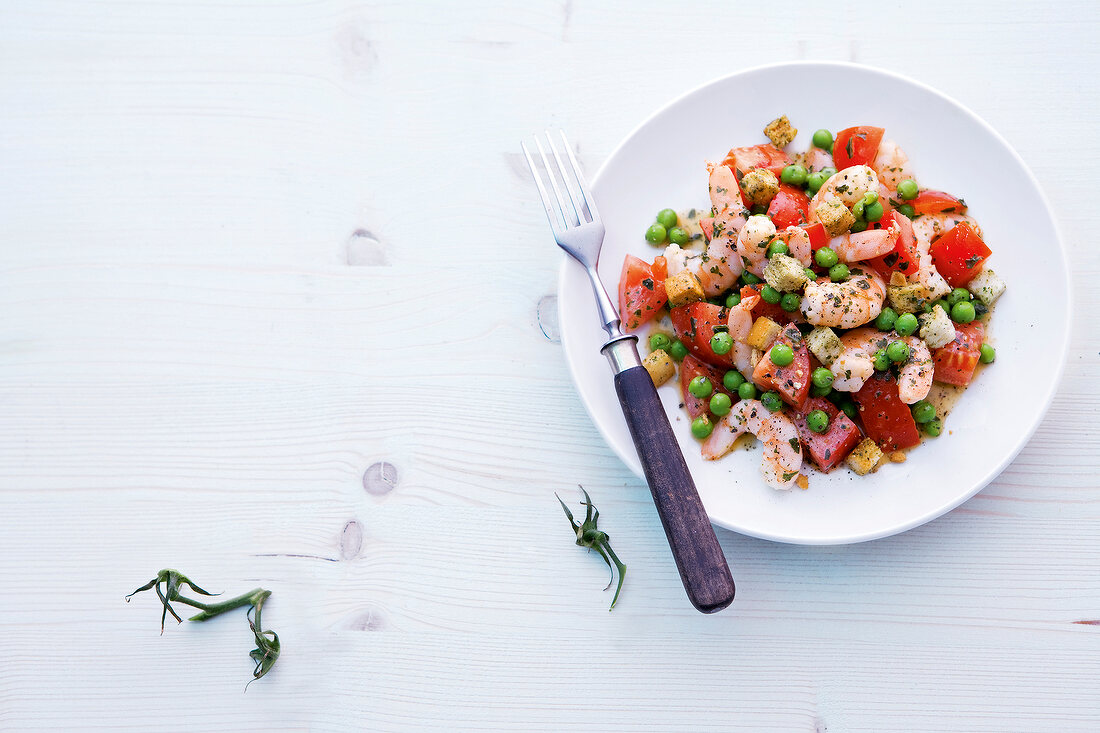 Tomato salad with peas and shrimp on plate with fork